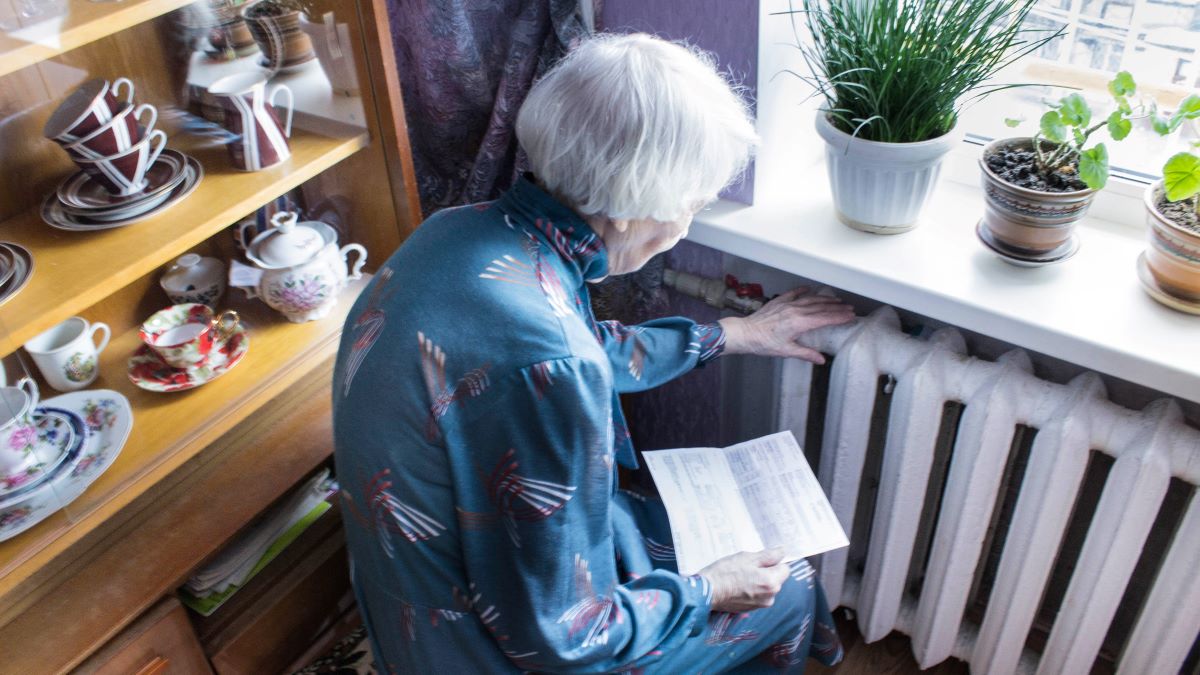 elderly woman sitting beside radiator with electricity bill