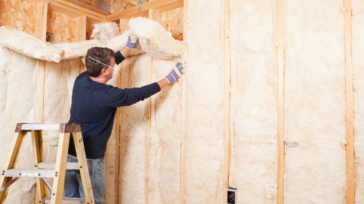 man installing wall insulation on ladder