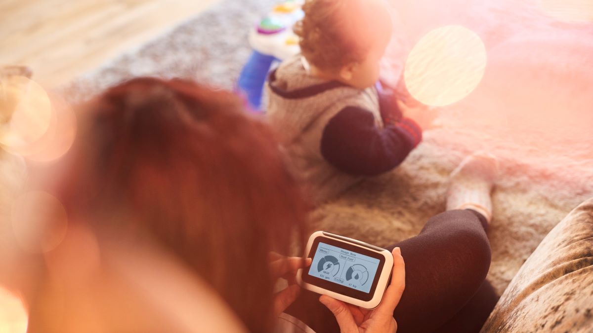 woman looking at a smart meter display while child plays in front of her