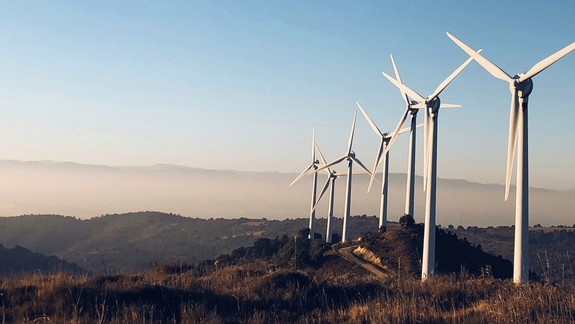 windturbines on hillside with blue sky behind