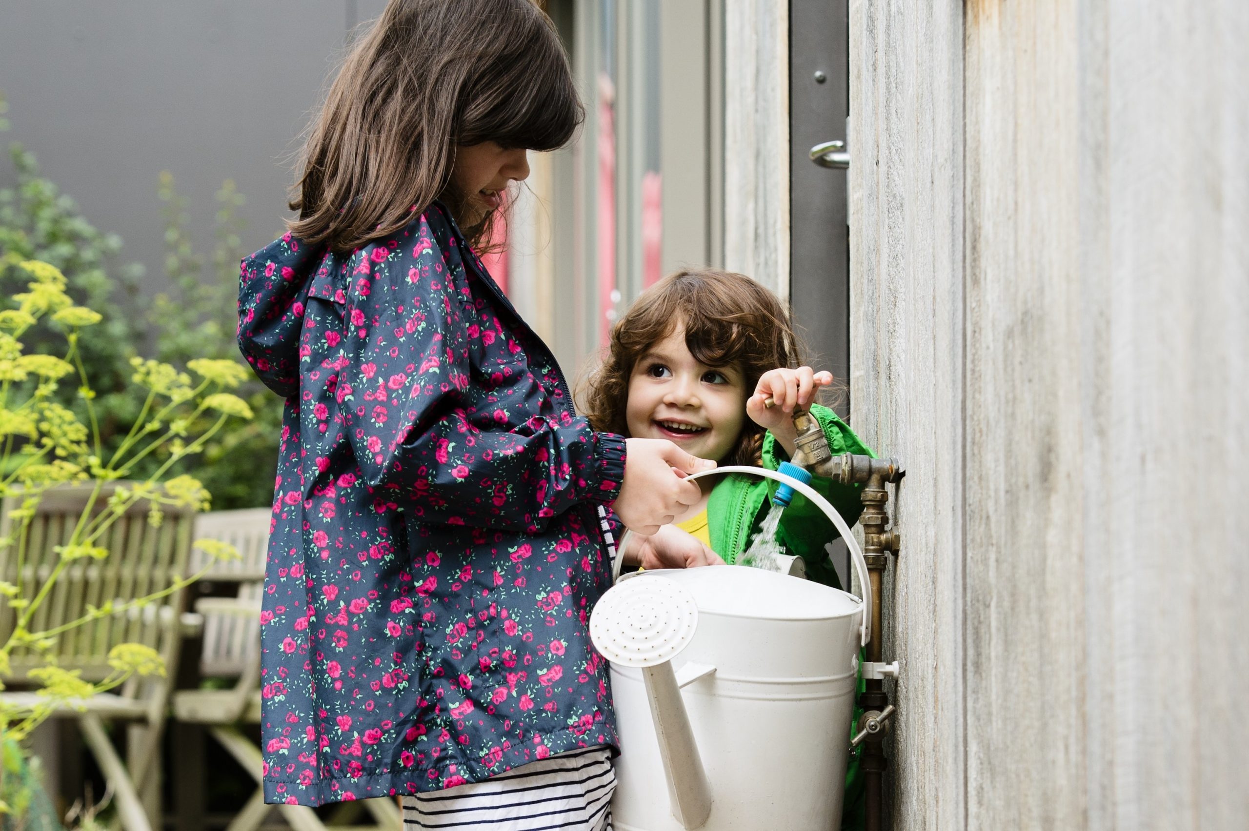 Two children collect rainwater into a watering can