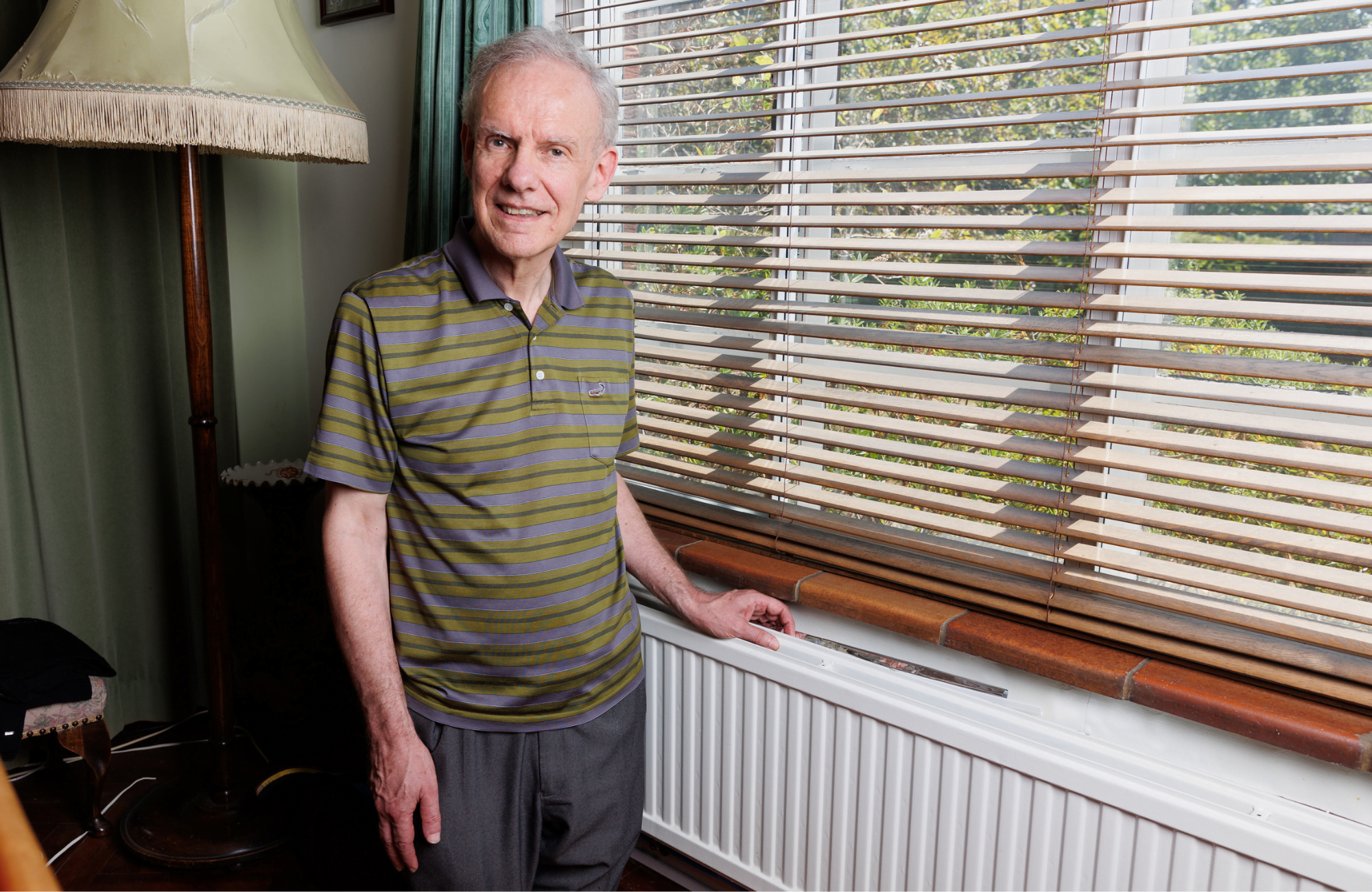 Peter stood in front of a window with his hand on a radiator underneath the window.