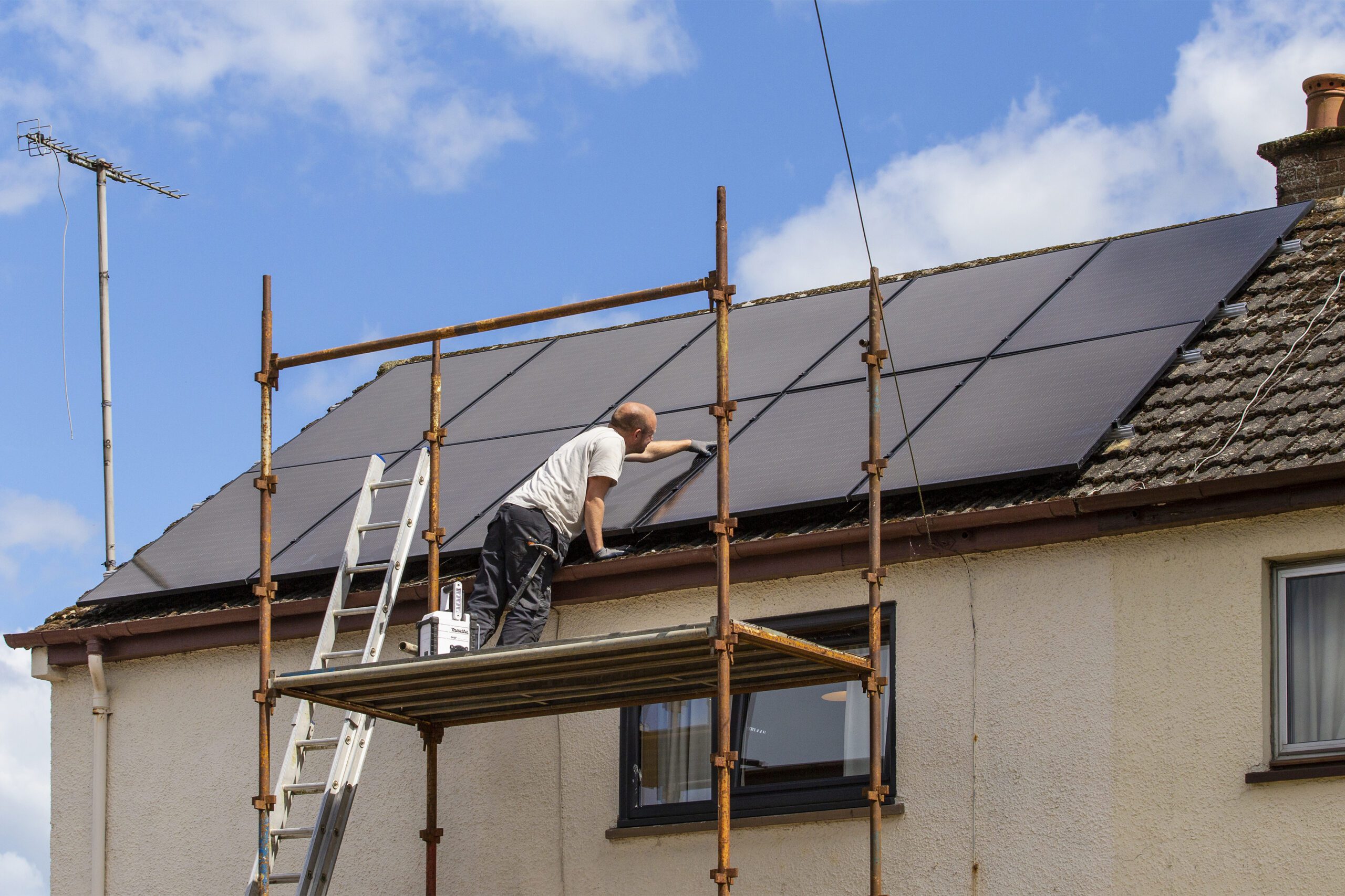 Man stands on scaffolding installing solar panels on a roof.