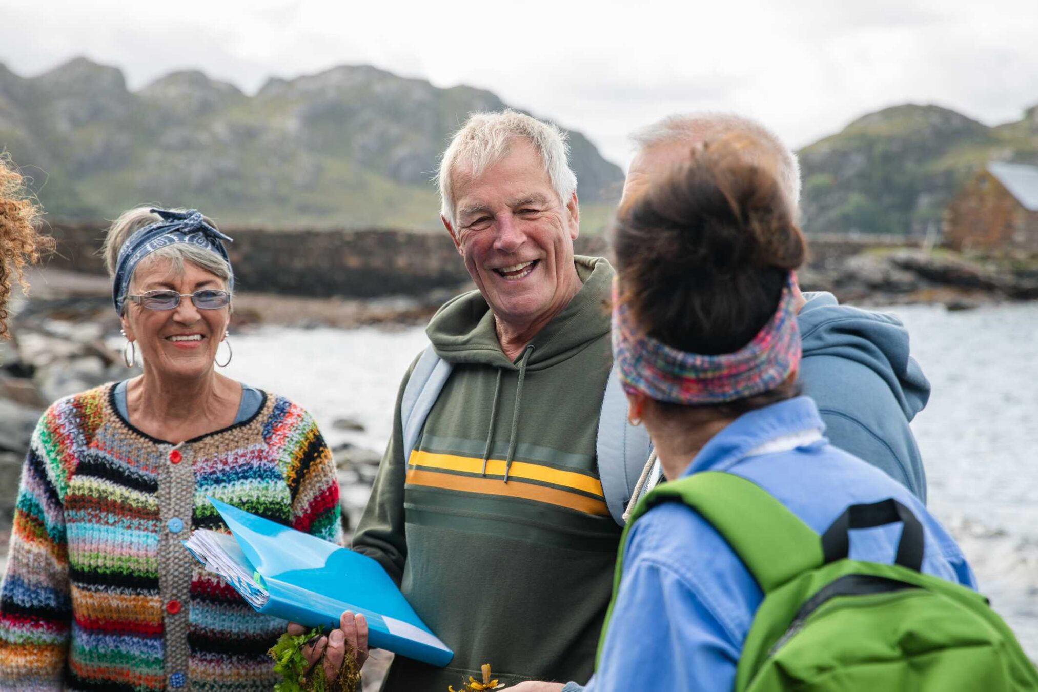 A group of older men and women smiling and chatting by a shoreline