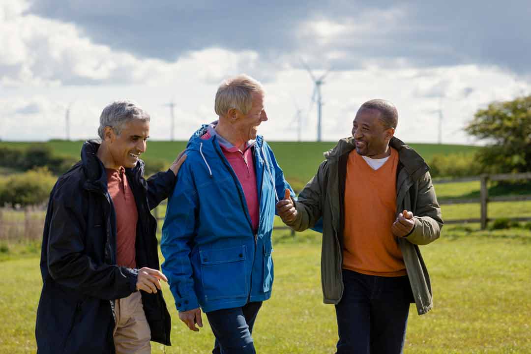 Three men wearing jackets in a field with wind turbines in the background.