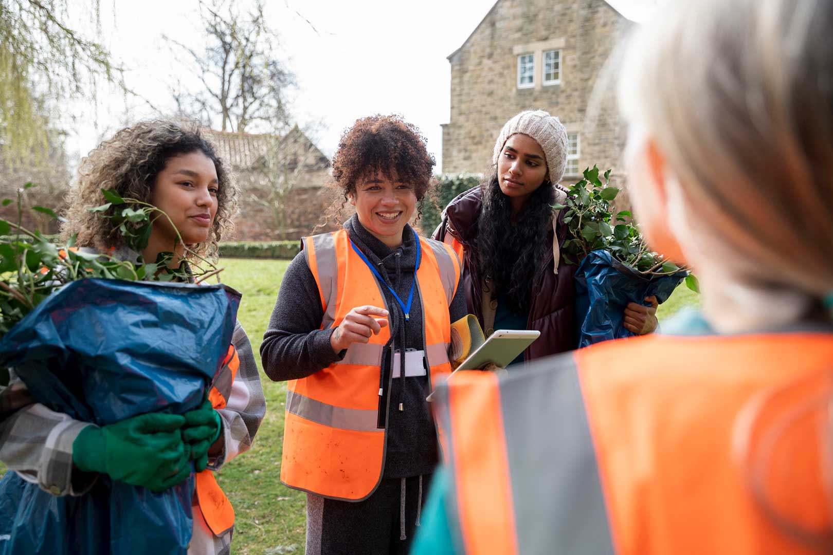 A group of people wearing hi vis jackets stood outside. The leader of the group is holding a tablet.