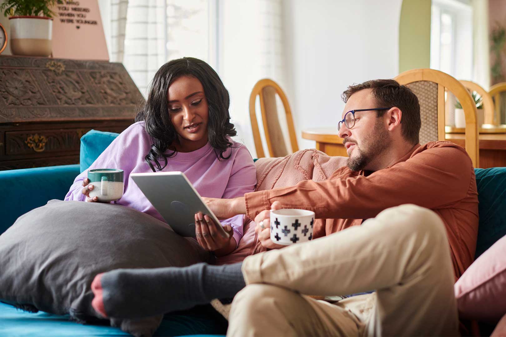 A couple sat on a sofa using a digital tablet.