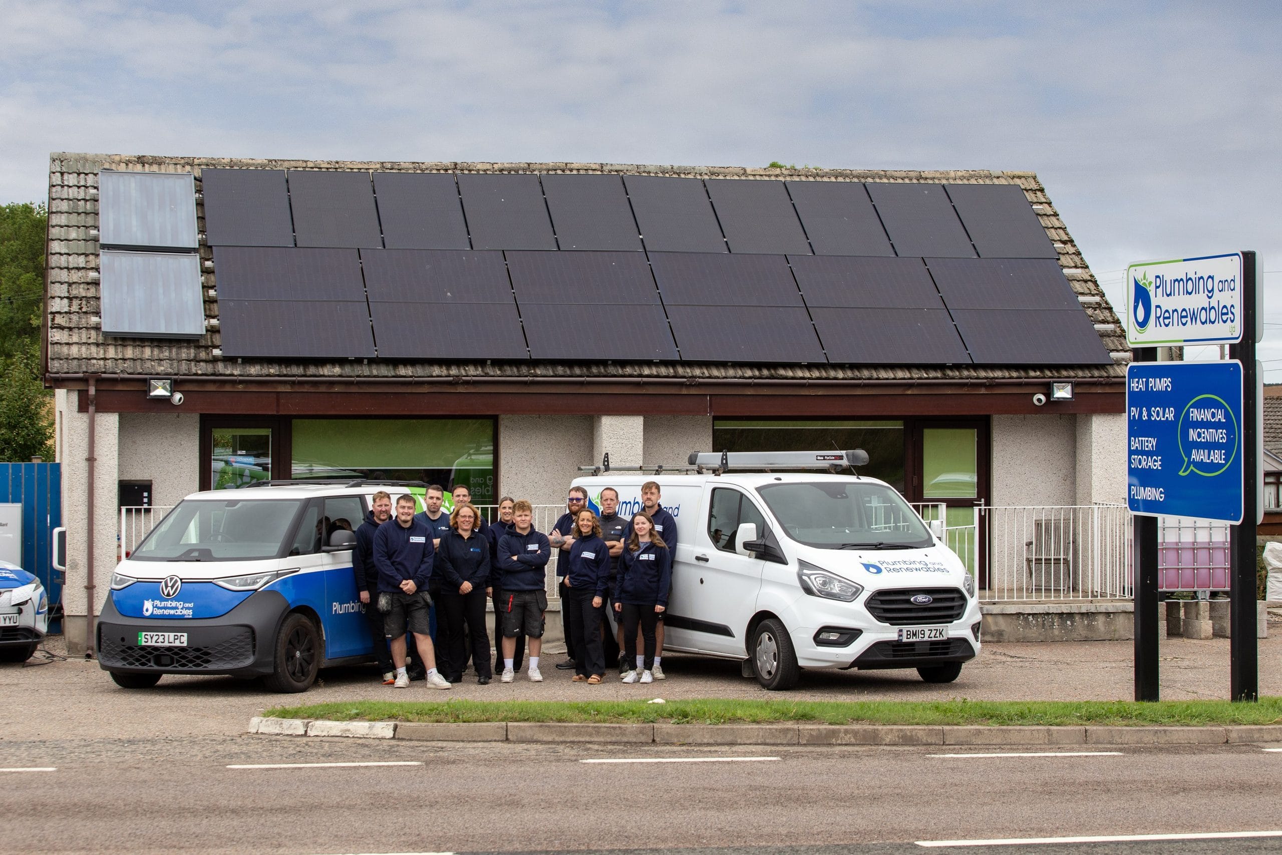 Group in uniform outside building with solar panels and company vans, under 