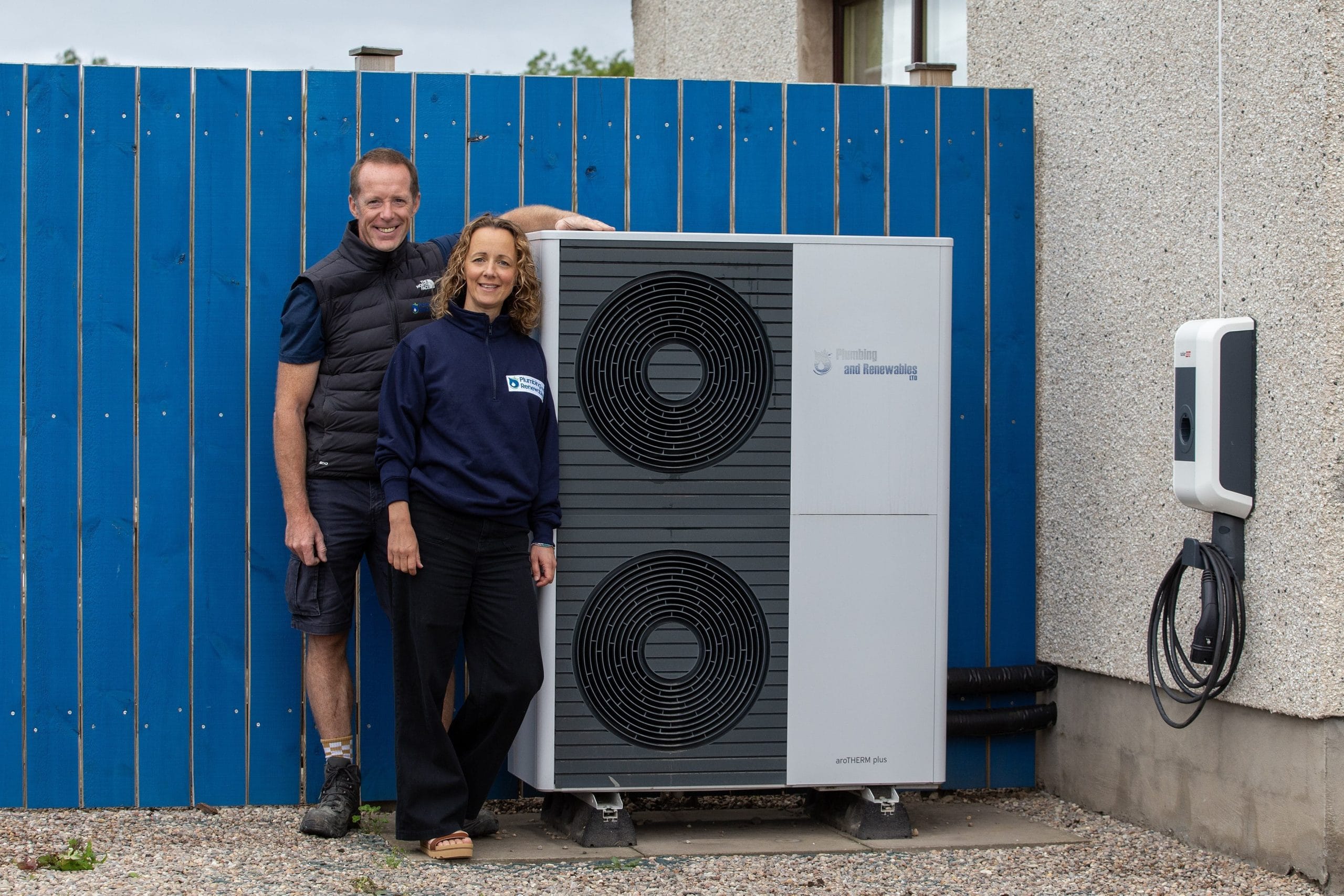 Two people beside a large heat pump unit outside a building.