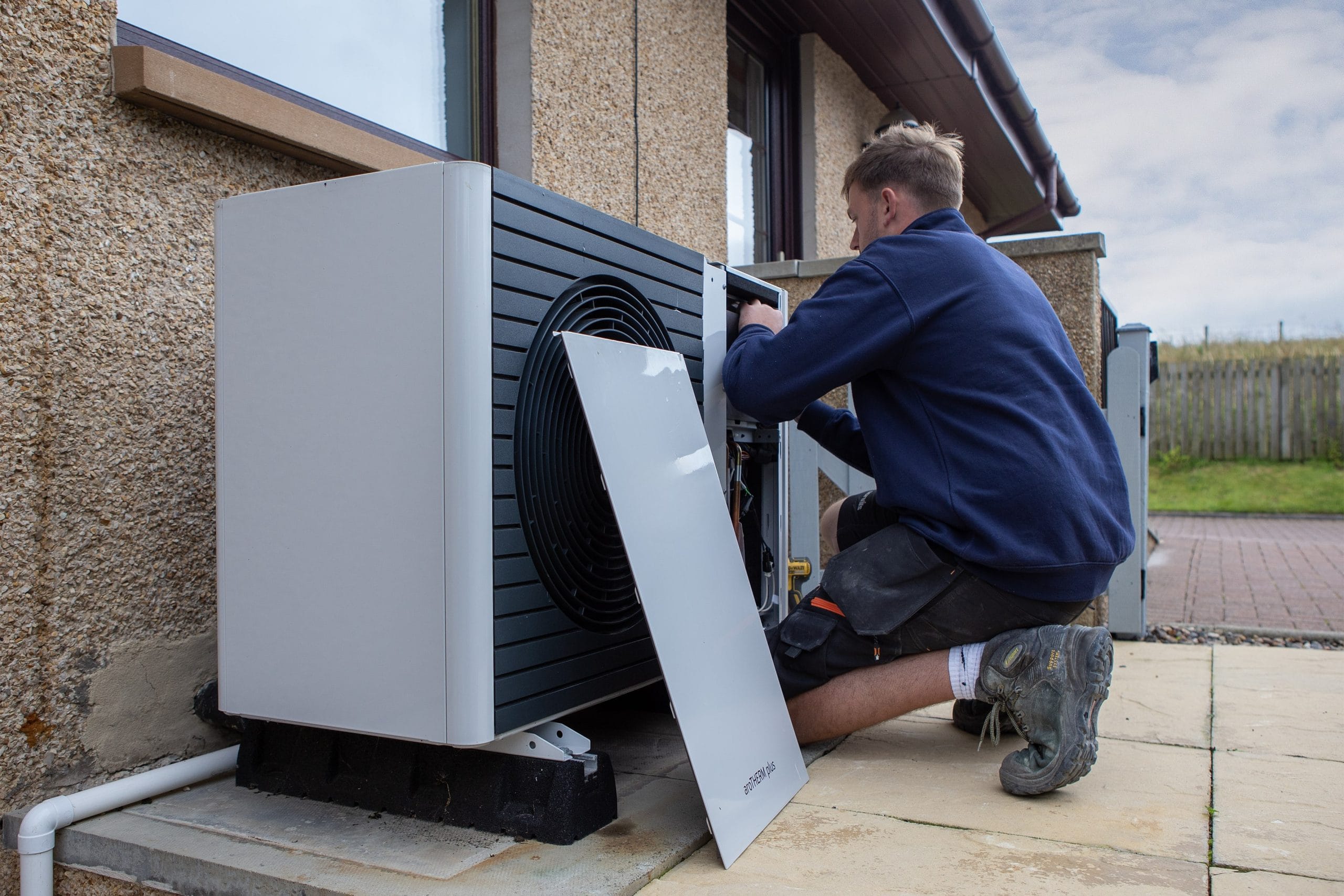 Technician kneeling outside, working on a heat pump unit