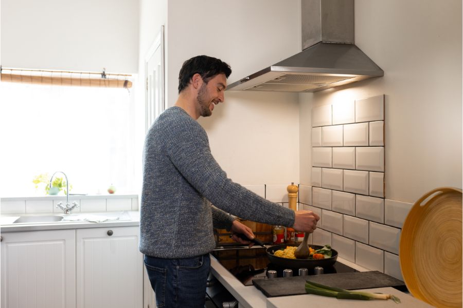Man in kitchen cooking food on the rear hob while using the cooker extractor hood.