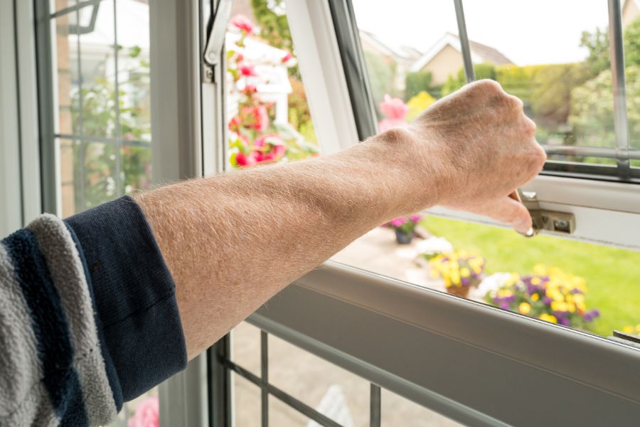 Homeowner opening a double glazed window seen on the ground level of a property to improve ventilation.
