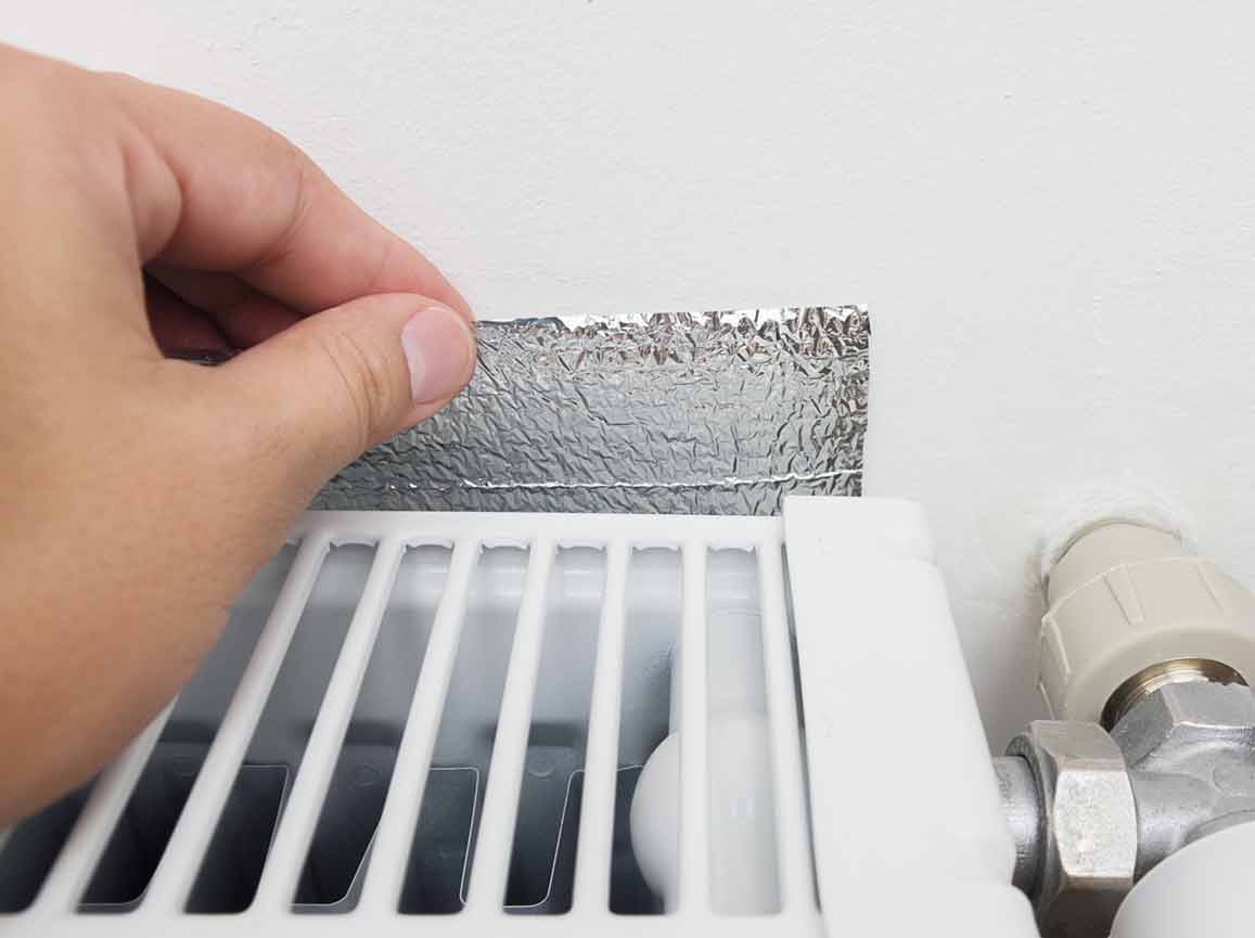 Someone placing a radiator reflector panel behind a radiator.