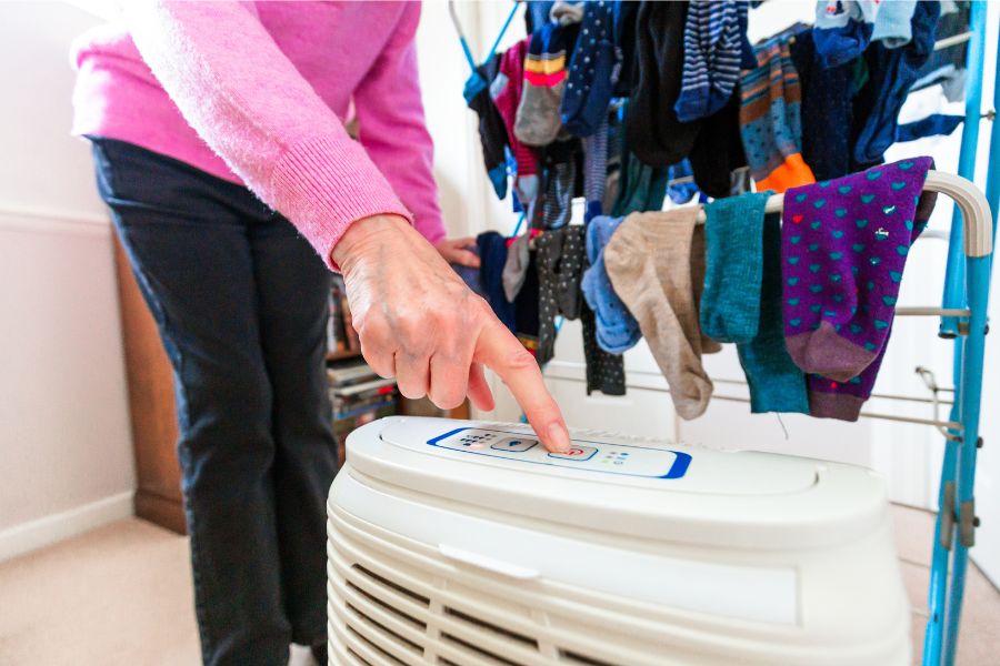 Woman switching on dehumidifier while drying laundry at home.