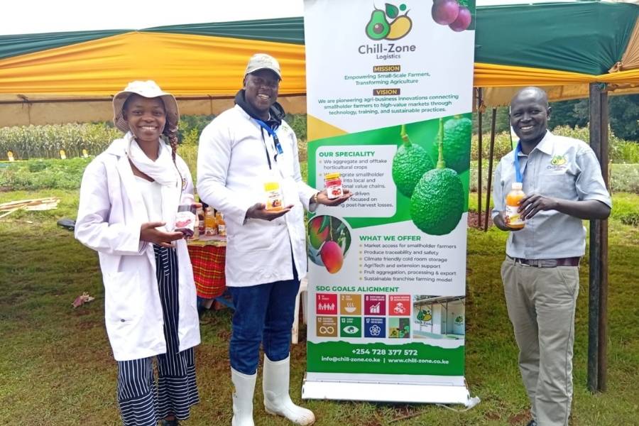 Three people standing in front of a Chill‑Zone Logistics display banner while holding packaged agricultural products at an outdoor event.