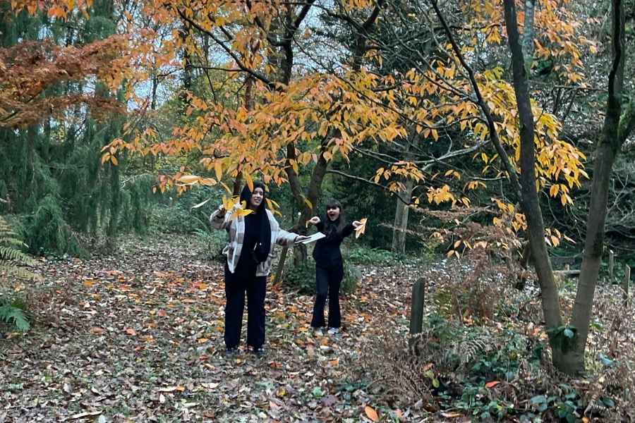 Two people standing in the woods beneath a tree.