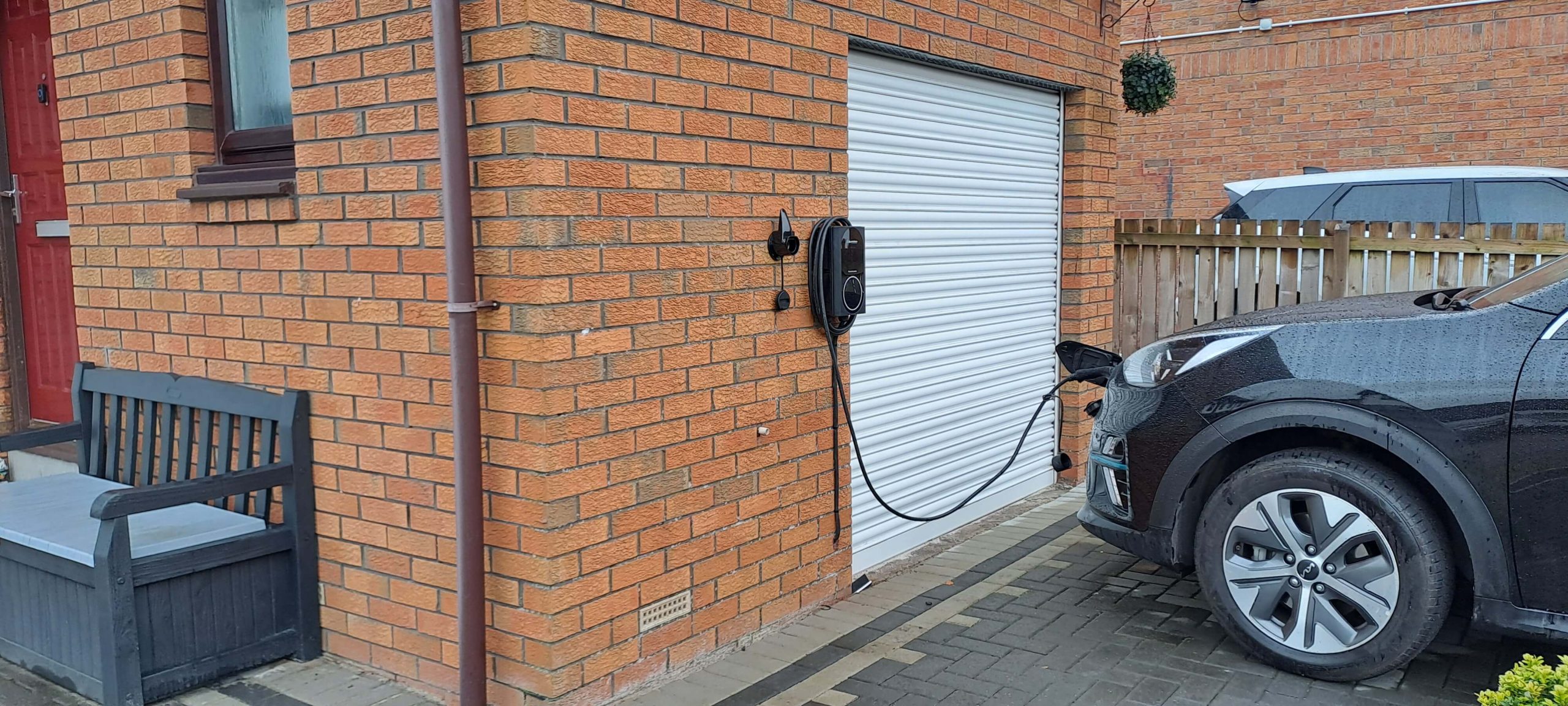 A home charge point plugged into a car on the driveway
