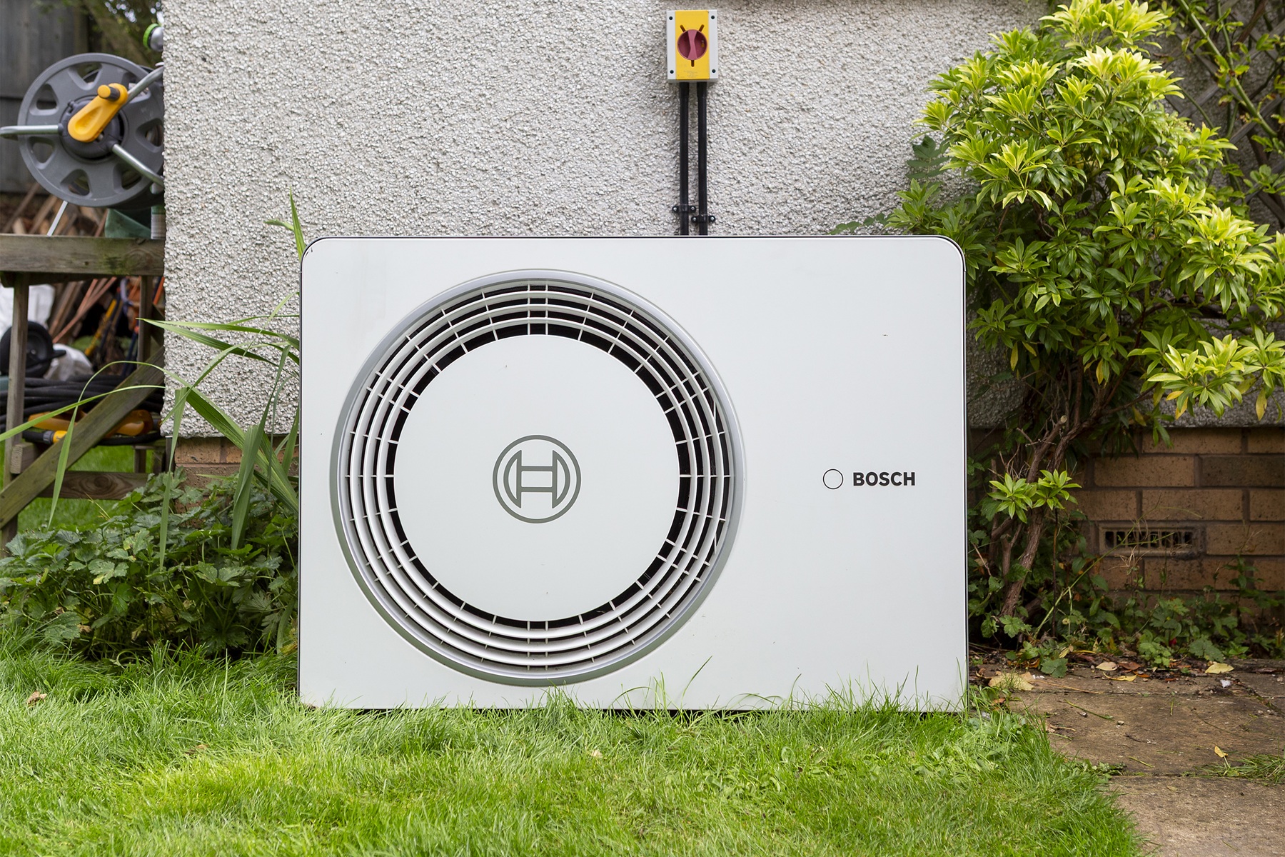 Bosch outdoor heat pump unit installed next to a house with surrounding greenery.