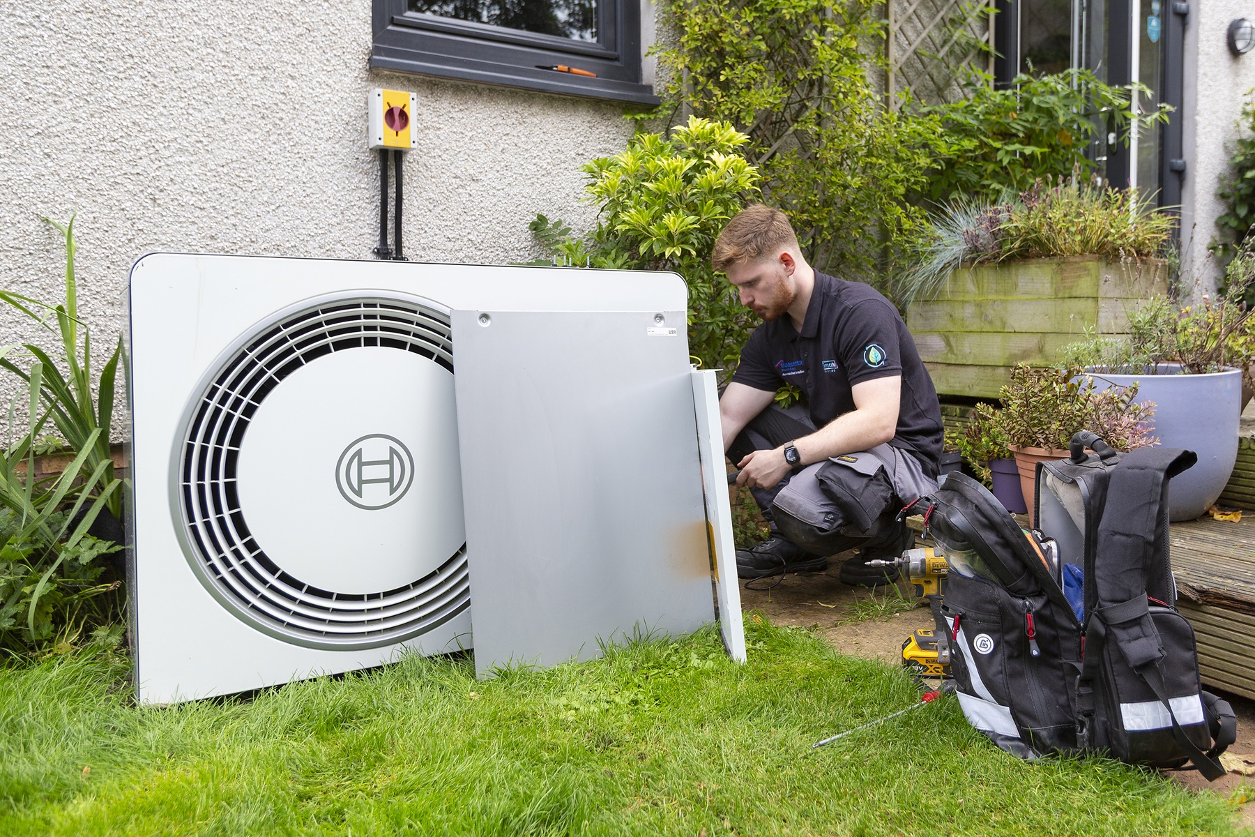 Installer working beside an outdoor Bosch heat pump unit mounted against the wall of a house.